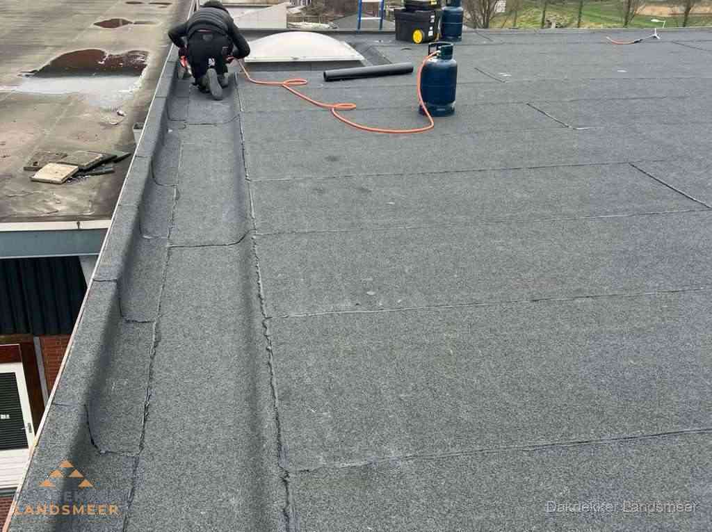 Dakdekker repareert bitumen dakbedekking op groot plat dak in Landsmeer